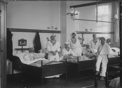GN2623 Groepje mannen in een ziekenzaal van het Marinehospitaal. Een van hen houdt een exemplaar van Het Volk omhoog; ...