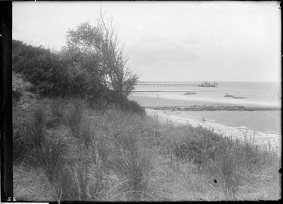 GN2672 Kijkje op de duinen, het strand en de Noordzee. Langs het aanlegsteiger ligt de veerboot; ca. 1925