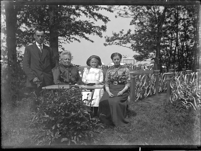 GN3152 Gezin rond de tafel in de tuin, op de achtergrond de kermis (2e van links mevr. Boers-Cording); ca. 1914