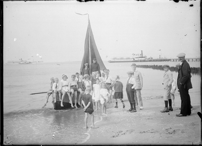 GN5093 Kijkje op het Strand van Oostvoorne, een groepje kinderen staat rond een zeilboot; ca. 1920