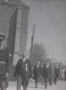 B1070 Een stoet hoogwaardigheidsbekleders loopt langs de kerk; een man draagt een bodebus; ca. 1950