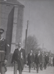 B1070 Een stoet hoogwaardigheidsbekleders loopt langs de kerk; een man draagt een bodebus; ca. 1950