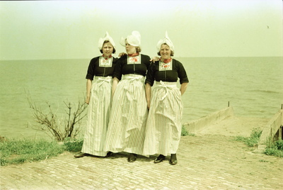 NL-PmWA-CRH_195400003 Drie jonge vrouwen op de dijk in Volendam in traditionele klederdracht.