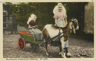 P-1262 Walchersche Kleederdracht (Zeeland). Uit rijden. Twee meisjes in Walcherse dracht op een bokkenwagen.