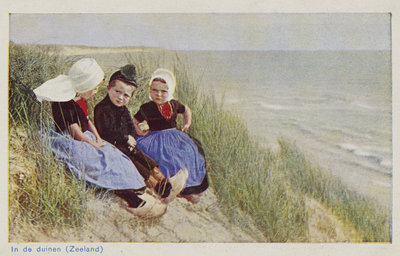 P-1365 In de duinen (Zeeland).. Drie kinderen in Zeeuwse dracht zittend in de duinen.Jongen draagt zogenaamd pluumpetje.