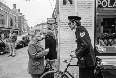228 Een vrouw en een politieagent bij de fotohandel van L. Helder op de hoek van de Lange Delft en de Sint Janstraat te ...