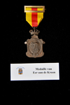 64 Medaille van Eer aan de Kroon. Dit is een bronzen medaille in de vorm van een afgerolde oorkonde met een kroon. Aan ...