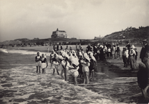 2343 Een groep meisjes in Walcherse klederdracht met de rokken omhoog op het strand van Domburg, met toeschouwers