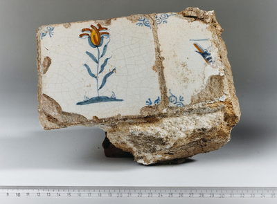 868 Brokstuk van een muur met wandtegels, waarop een bloem is afgebeeld