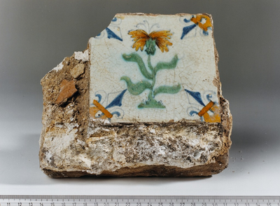 874 Brokstuk van een muur met wandtegel, waarop een bloem is afgebeeld