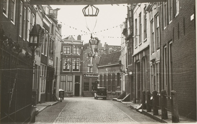 1954 Gezicht in de Kapoenstraat te Middelburg met versiering voor Koninginnedag of een jubileum van de koningin, met op ...