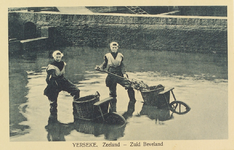 5960 Yerseke. Zeeland - Zuid-Beveland. Twee poserende oesterwerksters in een oesterput in Yerseke, met een vork, ...