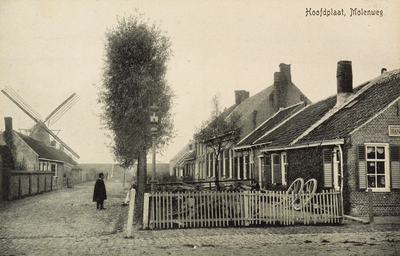 8361 Hoofdplaat, Molenweg. Gezicht op de Molenweg met molen te Hoofdplaat; rechts liggen een paar wagenwielen tegen het huis