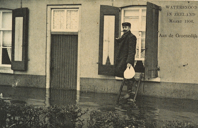 8904 Watersnood in Zeeland Maart 1906. Aan de Groenedijk. Een man op een laddertje voor een onder water gelopen woning ...
