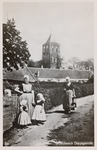 9181 Walchersch Dorpsgezicht. Een paar vrouwen en meisjes in Walcherse dracht met op de achtergrond de kerktoren van ...