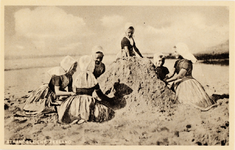 9243 Strandgezicht, Zeeland. Een zestal meisjes in Walcherse dracht spelen op het strand in het zand