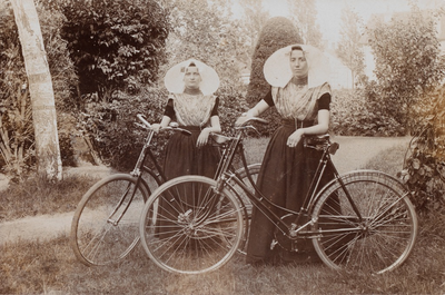 9347 Twee vrouwen in protestantse, Zuid-Bevelandse dracht poseren in een park met hun fiets