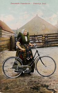 9406 Zeeuwsch - Vlaanderen - Oostelijk Deel. Een meisje in Axelse dracht poseert met haar fiets op het erf van een boerderij