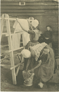455-1263 Twee vrouwen in dracht bezig met het ophangen van wasgoed