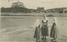 455-539 Strand te Domburg. Drie meisjes in dracht op het strand te Domburg met op de achtergrond het Strandhotel