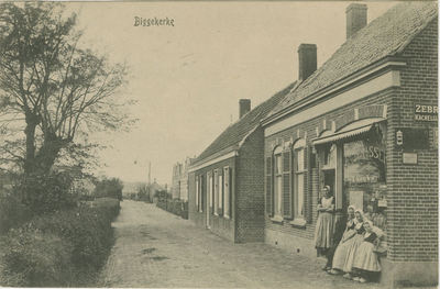 455-587 Biggekerke. Een vrouw en vier kinderen in dracht voor de kruidenierswinkel De Kleine Winst aan de Valkenisseweg ...