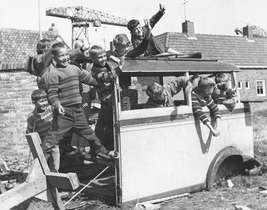 605-6-106 Jongetjes spelen in een wrak van een oude bus te Vlissingen. Op de achtergrond twee kranen van scheepswerf De ...