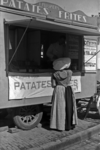 895-12 Vrouw in Zuid-Bevelandse dracht bij de kraam met patates-frites van J. Pluijmers op de Markt te Middelburg