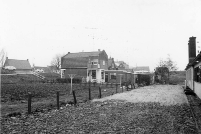 B-1490 Bruinisse. Boomdijk. De achterkant van de huizen aan de Boomdijk, met rechts een barak van het werkkamp in de ...