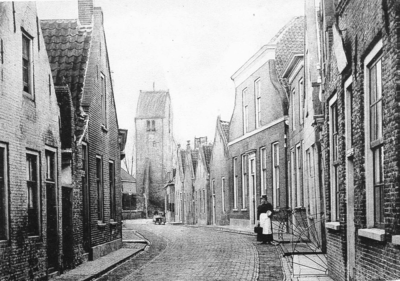 D-0574 Oosterland. Kerkstraat gezien vanuit het noorden. Op de achtergrond de laat 14e eeuwse kerktoren met zadeldak.