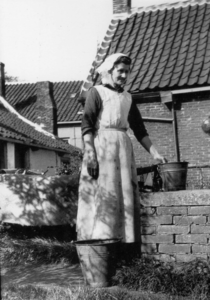 SP-0723 Schouwen-Duiveland. Vrouw met aek muste (gehaakte muts) bij de tras (regenbak) met pikketel (emmer)