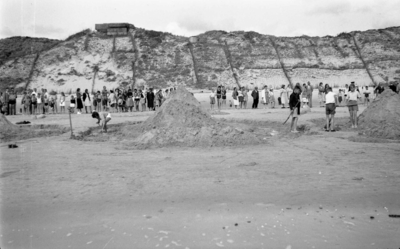 STO-0186 Westenschouwen. Strand. Wedstrijd zandkastelen bouwen met veel toeschouwers. Op het linkerduin de restanten ...