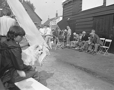 BE-1382 Dreischor. Oudere dorpsbewoners zitten tegen een typerende dorpsschuur met wanden van zwart geteerde planken. ...