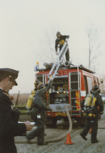 890235 Brandweerlieden met persluchtmaskers halen een ladder van een brandweerauto tijdens een brandweeroefening te ...