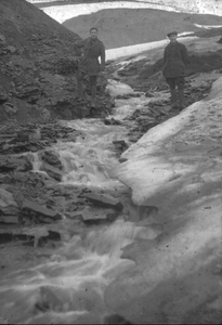 23-13-97 Twee jonge mannen in een bergachtig landschap met water en ijs op Spitsbergen