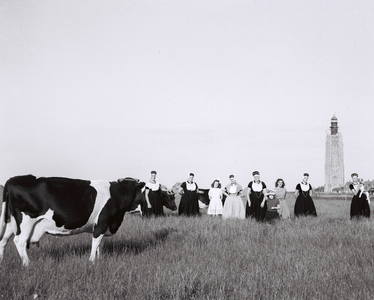 559 NFR Een groep vrouwen in dracht uit Westkapelle met een koe en op de achtergrond de toren van Westkapelle.