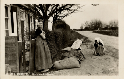 13224 'Zeeland, Walcheren, Spelende kinderen' Twee kinderen en vrouw in klederdracht bij een boeren woning