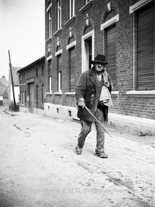 ehc_gp_140 Boer onderweg met wandelstok en lege zak op zijn schouder in een onbekend dorp in het Limburgse landschap
