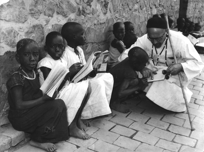 140031 Missionaris Perraudin geeft jeugdige catechumenen leesles in de openlucht in Burundi