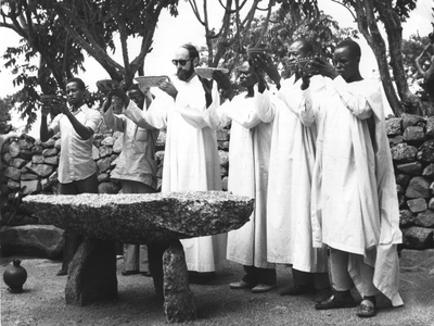 140032 Missionaris draagt (op een oude heilige plaats) gaven op aan de vruchten der aarde en bijbehorende arbeid in Kameroen