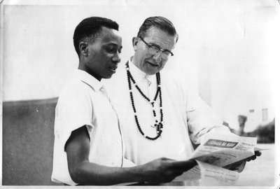 140044 Pater Leo Aarden leest met een Afrikaanse reporter wat deze jongeman in zijn krant geschreven heeft