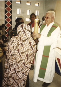 140056 Pater Nico de Bekker overhandigd een brandende kaars aan een stel tijdens een viering in Tanzania
