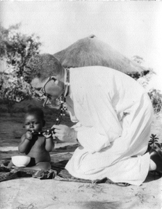 140193 Pater Ad van der Hout met een Tanzaniaanse peuter, die sabbelt aan zijn rozenkrans