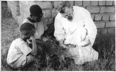 140232 Pater Bastiaan Jongerius bekommert zich met twee Afrikaanse jongens om een antilopenjong in Tanzania