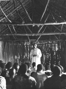 140380 Pater Leo Michielsen tijdens een gebedsdienst in een kerk van takken, bladeren en riet in Afrika