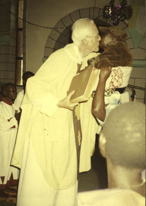 140435 Pater Hans Peters kust na de evangelie-lezing de bijbel en een kindje in de dagmis van Kerstmis te Maramba in Uganda