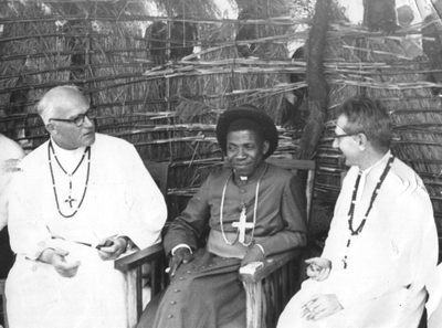 140485 Pater Bart Sleutjes en pater Steinkamp met bisschop C. Msakila kijken naar een dans in de missie van Tanzania