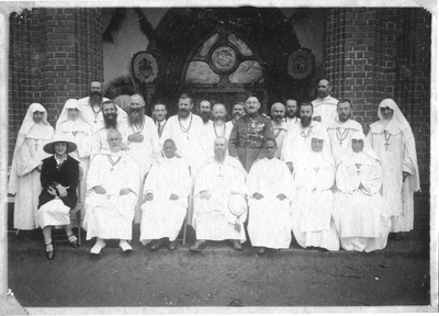 140663 Groepsfoto van pater Bernard Zuure met mgr. Gorju, medebroeders, Witte Zusters en notabelen voor de kerkingang ...