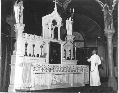 186635 Koster frater Lucianus bij het hoogaltaar van de kathedraal Sint Petrus en Paulus te Paramaribo (Suriname)