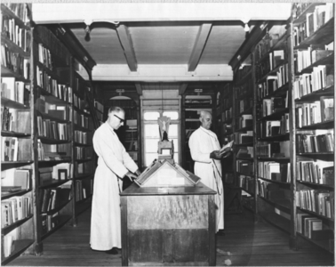 186649 Paters Dresen en Klinkhamer in de bibliotheek van de grote pastorie te Paramaribo (Suriname)
