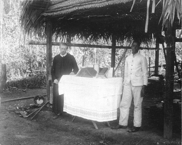 186862 Plantage altaartje met priester en misdienaar, tevens kok, in een Indianenkamp (Suriname)